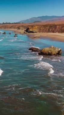 Sahile vuran güzel dalgaların büyüleyici görüntüsü. Kaliforniya 'nın merkez kıyısındaki Morro Körfezi' nin güneşli manzarası. Dikey video.
