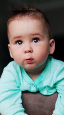 Yeşil gömlekli bir bebek kameraya bakıyor. Bebeğin küçük bir ağzı var ve komik bir ifade takınıyor.