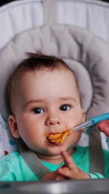 Yemek saatinde erkek bebek beslenmesi. Sevimli bebeğe yemek veriliyor ve el sallıyor ve dilini gösteriyor. Dikey video.