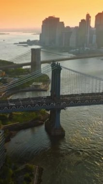 Manhattan ve Brooklyn Köprüleri, East River üzerinde. New York gökdelenlerinin siluetleri turuncu gökyüzünün arka planında. Dikey video.