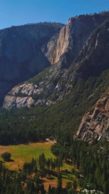 Yosemite Ulusal Parkı, Kaliforniya, ABD 'deki kayaların arasında çam ağacı olan güneşli bir vadi. Yukarıdan bakıldığında doğanın çarpıcı bir görüntüsü. Dikey video.