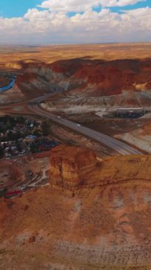 Saf sarı kayalarla çevrili sıcacık bir şehir. Çölün ortasından dağlara giden yol. Arka planda bulutlu bir gökyüzü. Dikey video.