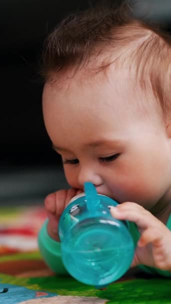 小さな赤ちゃんはボトルを扱うのに忙しい 素敵な髪型の素敵な子供は一人で水を飲もうとしています クローズアップ バーティカルビデオ — ストック動画