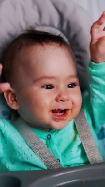 活発な健康な白人少年がスプーンを食べている かわいい子供が椅子に座って手を振る バーティカルビデオ — ストック動画