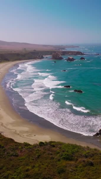 美丽的催眠泡沫波到达沙滩 岩石海岸覆盖着青草 有些石头从水里渗出 空中风景 垂直录像 — 图库视频影像