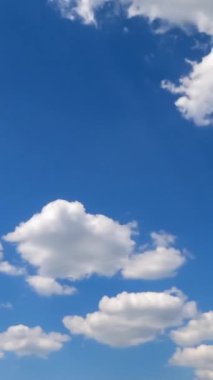 Mavi gökyüzünde yumuşak, güzel bulutlar oluşuyor. Bulutlar güneş ışınlarında hızla uçuyor. Zaman ayarlı. Dikey video.