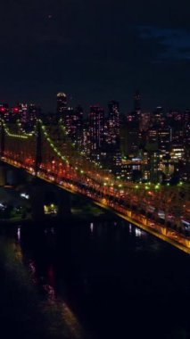 Muhteşem Queensboro Köprüsü yeşil ve turuncu ile aydınlatıldı. Gece vakti New York 'un ışıklarla dolu manzarası. Üst Manzara. Dikey video.