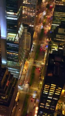 New York mimarisindeki binaların çeşitliliği. İnsansız hava aracı çok şeritli bir yolda gökdelenlerin arasından yavaşça iniyor. Dikey video.
