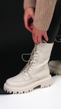 Dişi, traktör tabanındaki beyaz botları çeker ve dili tutar. Modern sonbahar ayakkabılarını gösteren bir model. Dikey video.
