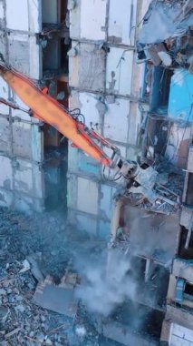 Mahvolmuş bina, özel makinelerin yardımıyla yıkılıyor. Koca Pençe yıkılmış binanın yerlerini mahvediyor. Enkaz düşüyor ve toz yükseliyor. Dikey video.