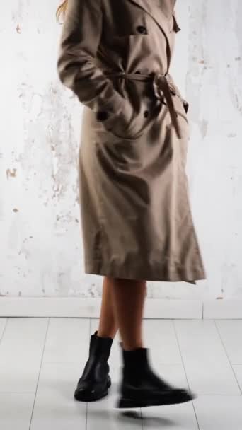 モダンな服とスタイリッシュな靴のデモンストレーション スタジオでポーズするベージュコートとブラックトラクターブーツを着用したモデル バーティカルビデオ — ストック動画