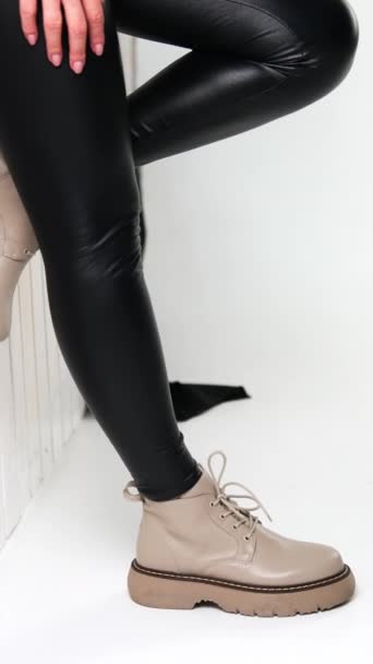 穿着黑色皮裤 米黄色毛衣和靴子的模特靠在墙上 女性展示了现代时尚的外表 垂直录像 — 图库视频影像