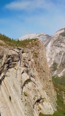 Yosemite Ulusal Parkı 'nın dik gri uçurumları, Kaliforniya, ABD güneşli bir günde. Havadan bakıldığında çam ağaçlarıyla kayalık bir manzara. Dikey video.