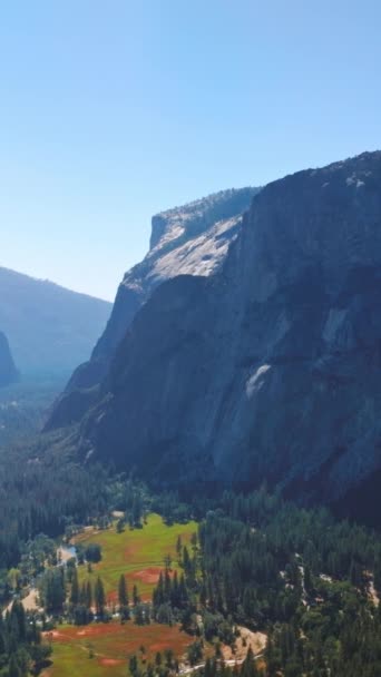 アメリカ合衆国カリフォルニア州ヨセミテ国立公園の山々の間で日光を浴びた木造の谷 青空の背景にある豪華な岩の美しい景色 バーティカルビデオ — ストック動画