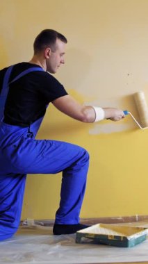 Genç adam dairesini yenilerken duvarları fırçayla boyuyor. Tamir, bina ve ev konsepti. Dikey video.