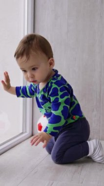 Güzel beyaz bebek merakla pencereye bakıyor. Odanın zemininde hareket eden güzel bir çocuk. Dikey video.
