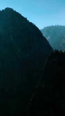 Tepesinde ağaçlar büyüyen iki yüksek kaya. Yosemite Ulusal Parkı 'ndaki sisin içindeki güzel dağlar, Birleşik Devletler. Dikey video.