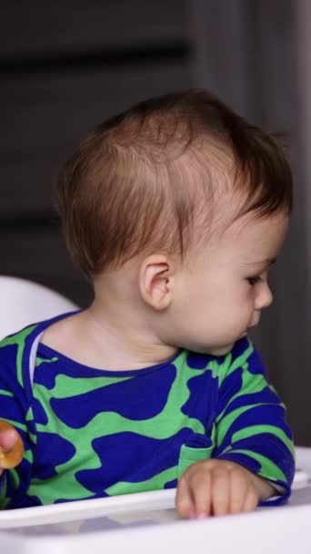 可爱的小孩穿着蓝绿相间的衬衫坐在餐桌旁 妈妈正在给她的孩子一个大勺子 他拿去了 模糊的背景 垂直录像 — 图库视频影像