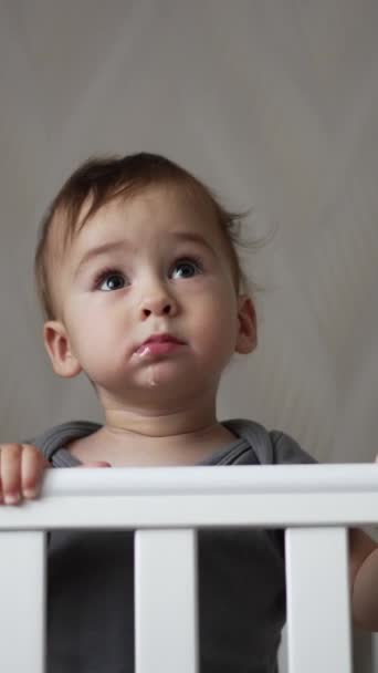 迷人的漂亮男婴站在他的婴儿床里 可爱的白人小孩带着华丽的笑容露出两颗下颌牙 垂直录像 — 图库视频影像