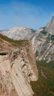 Parlak güneşle aydınlanan dikey kaya oluşumları. Yosemite Park, California, ABD 'deki dağların eteklerinde çam ağacı ağaçları yetişiyor. Dikey video.
