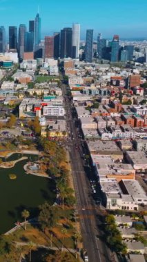 Şehrin sık mimarisinin arasında yeşil hoş bir park. Güneşli Los Angeles 'ın panoramasında güzel gökdelenler var. Üst Manzara. Dikey video.