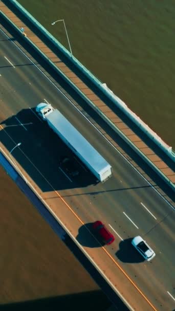 片道の複数車線の高速道路で橋で移動する車の後 グリーンウォーターの背景にある橋の上の晴れた映像 トップビュー バーティカルビデオ — ストック動画