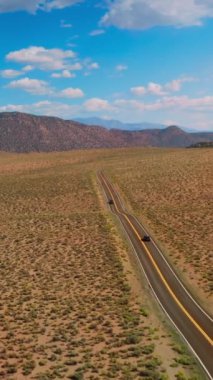 Nevada 'nın güzel dağlarına giden otoyol çöl boyunca uzanıyor. Sıcak ve güneşli bir günde göz kamaştırıcı manzara. Hava görüntüsü. Dikey video.