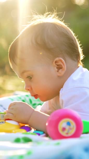 素敵な小さなコーカサス トッドラーは庭の平原に腹の上に横たわっています 明るい太陽の光線でおもちゃを見ている素敵な子供 バーティカルビデオ — ストック動画