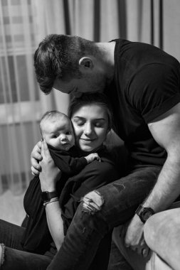 Genç bir aile kanepede oturuyor ve yeni doğmuş bebeklerini kucaklıyorlar..