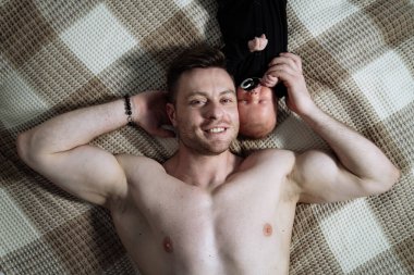 Genç baba yeni doğmuş bebeğiyle yatakta yatıyor ve gülümsüyor..