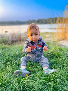 Küçük çocuk çimenlerde oturur ve kameraya bakar..
