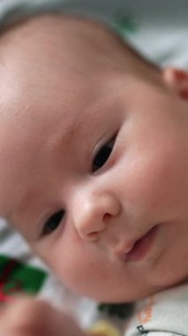 Hoş bir çocuk ellerini yüzünün önünde hareket ettiriyor ve onları takip ediyor. Sevimli çocuk yatakta yatarken eğleniyor. Kapatın. Dikey video