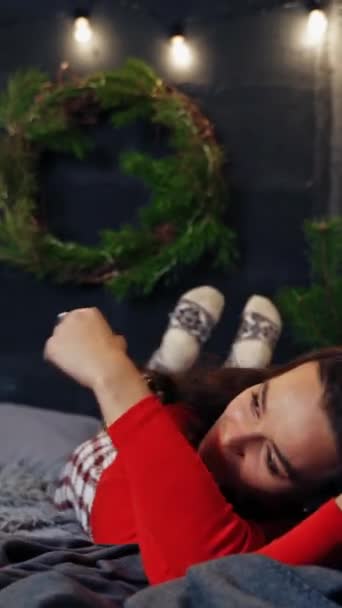 新年のベッドに横たわる陽気な女性 クリスマスの装飾された部屋の背景に喜んでベッドの上に転がるかなり笑顔の若い女性 バーティカルビデオ — ストック動画