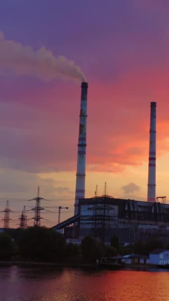 日没の産業エリア 美しいピンクの空に川の近くにある工場 煙による有害な製造は 夜の産業用パイプから行われます バーティカルビデオ — ストック動画
