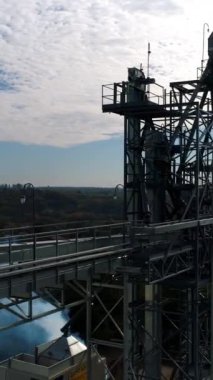 Endüstriyel fabrikanın tepesi Modern asansörler ve doğanın arka planında metal kule. Kırsaldaki büyük fabrikadan duman çıkıyor. Hava görüntüsü. Dikey video