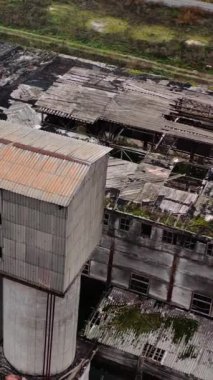Terk edilmiş eski bir bitki. Sahadaki hasarlı binalar. Kırık camlar ve yıkılmış bir fabrikanın çatısı. Hasarlı endüstri. Hava görüntüsü. Dikey video