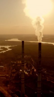 Doğada endüstriyel borular. Akşamları göl kenarında zararlı bir fabrika. Kimyasal duman gün batımında doğal atmosfere yayılır. Hava görüntüsü. Dikey video