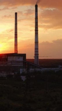 Akşamları fabrikada. Gün batımında havayı dolduran endüstriyel borulardan kirli emisyonlar. Ekolojik sorunlar. Hava görüntüsü. Kamera yükseliyor. Dikey video
