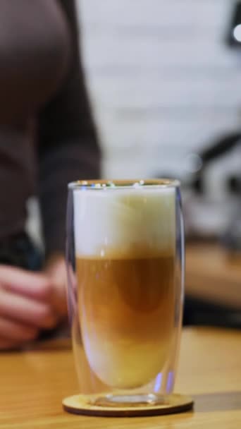 卡布奇诺或拿铁在玻璃中 女人把咖啡机里的水 新鲜咖啡 桌上放有奶油和高玻璃杯 垂直录像 — 图库视频影像