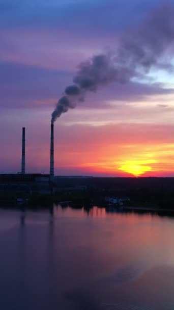 晚上在河边工厂附近 夕阳西下时 工业厂房散发出浓烟 让河流在化学制造背景下平静 空气污染 空中风景 垂直录像 — 图库视频影像