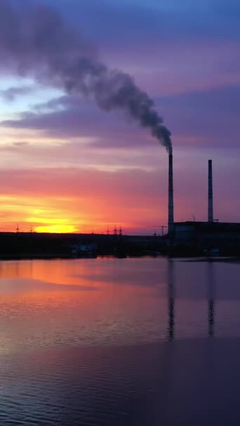 日落时河上的化工厂 晚上工业工厂向空气中排放有害的烟雾 摄像头升起了 垂直录像 — 图库视频影像