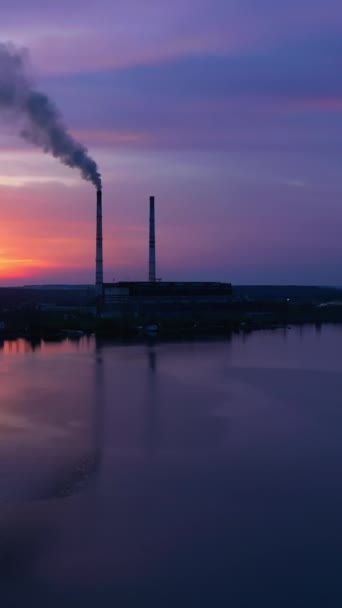 蓝色背景的河流和工业厂房 在夕阳西下 管子冒出的脏烟 日落时湖畔一家工厂的轮廓 垂直录像 — 图库视频影像