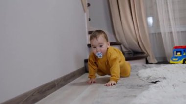 Ağzında emziğiyle odada hızla sürünen inanılmaz tatlı çocuk. Meraklı erkek bebek kameraya yaklaştı..