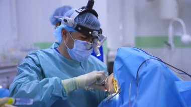 Kafasında cihaz gözlüğü olan konsantre cerrah enstrümanları dikkatlice takar. Modern cerrahide Otolaryngology operasyonu gerçekleştirildi.
