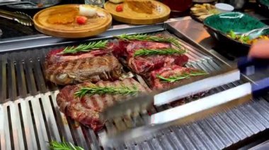 Aşçı ızgarada pişirirken et parçalarını çevirmek için barbekü maşası tutuyor. Akşam yemeği için lezzetli biftek hazırlığı..