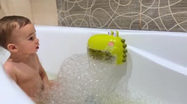 Beyaz çocuk küvette banyo yapıyor. - Ne? Küçük çocuk makineye dokunuyor kabarcıklar üretiyor ve düğmeye basıyor..
