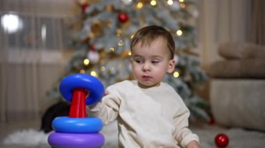 Oyuncak piramitle oynayan güzel bir çocuk. Siyah kedi çocuğun arkasından belirir ve kameraya doğru koşar. Arkaplanda bulanık bir Noel ağacı.