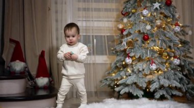 Beyaz pijamalı çocuk odanın önünden geçiyor. Çocuk elinde bir emzik tutuyor. Arkaplanda bulanık bir Noel ağacı.