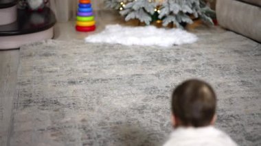 Odada emekleyen küçük çocuk. Sevimli erkek bebek elinde Noel süsleriyle merdivenlere yaklaşıyor..