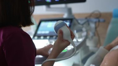 Doğum uzmanı sensörü tutuyor ve ultrason makinesinin tuşlarına basıyor. Doktor hamile bir kadının muayenesini başlatıyor..